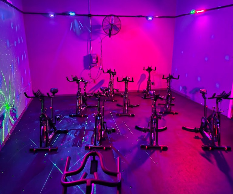 TBC Wellness Center spin studio with black-light cycle lighting.